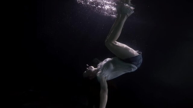 dressed woman is plunging in depth of pool or sea, underwater slow motion shot of female figure