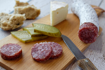 Close-up of a simple Bavarian snack. With Italian salami, a French soft cheese, pickled cucumbers and whole wheat rolls.