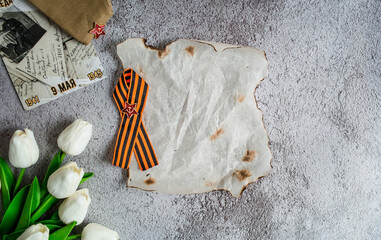 St. George ribbon, cap, tulips and burnt paper on a concrete background. The inscription in...