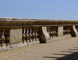textured beige stone balustrade guard rail. blue sky. abstract deminishing perspective view. yellow tile flooring. exterior terrace and observation deck structure.