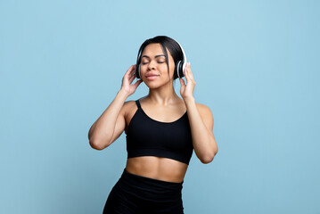 Naklejka premium Fit african american woman enjoying music at exercising during COVID-19 pandemic, blue studio background