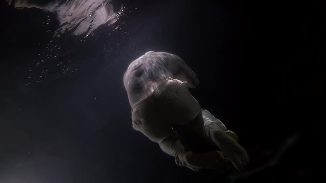 sunken man underwater, male figure is floating under water surface in darkness, ocean or aquarium