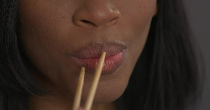 Cropped view of African woman eating Philadelphia sushi roll with salmon using chopsticks. Traditional Japanese cuisine.