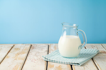 Milk jug on wooden table with tablecloth over blue background. Kitchen mock up for design
