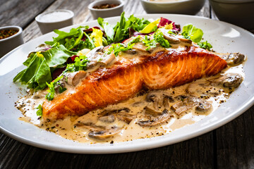 Fried salmon steak in mushroom sauce and vegetable salad served on wooden table
