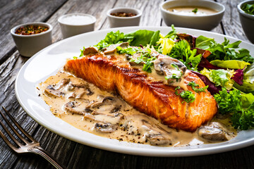 Fried salmon steak in mushroom sauce and vegetable salad served on wooden table

