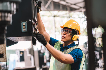 Work at factory.Asian worker man  working in safety work wear with yellow helmet and glasses l ear muff using equipment.male mechanical asia in factory workshop industry machine professional