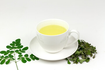 Moringa Tea in white cup with fresh and dry green leaf isolated on white background. Moringa oleifera tropical herb healthy lifestyle concept.