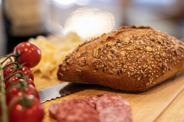 Seeded Bread roll with knife, cheese and cherry tomatos on a wooden bread board.