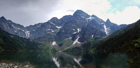 Wide angle view of Morskie Oko naturally formed lake pond in Tatra Mountains in Poland. High mountain landscape with dramatic clouds covered with snow and trees at national park High Tatras Europe
