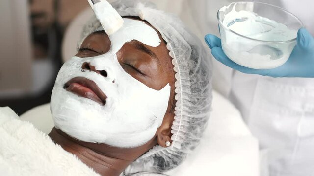 Cosmetologist applies alginate mask with spatula on face of woman