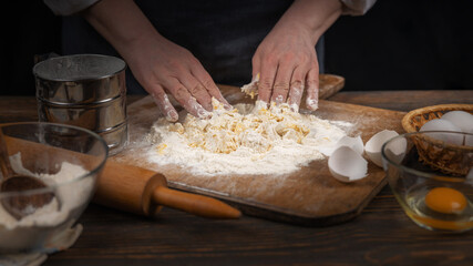 Women's hands, flour and dough. A woman in an apron prepares dough for homemade baking, a rustic home cozy atmosphere, a dark background with unusual lighting.