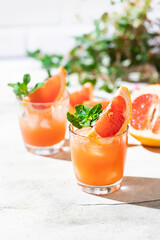 Cold cocktail of crushed ice with a slice of grapefruit on a light gray concrete background. Refreshing drink with ice.