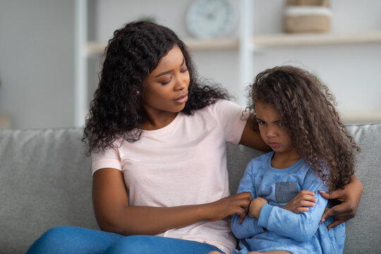 Young black mother comforting angry and upset little girl, hugging and consoling her at home. Solving family conflicts