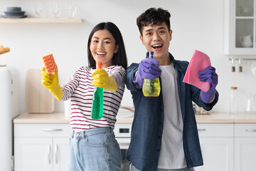 Cheerful asian couple with supplies for cleaning posing in kitchen