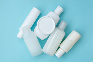 Set of different white plastic cosmetic bottles on blue background, abstract skin and body care, top view flat lay