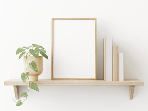 Small vertical wooden frame mockup in scandi style interior with trailing green plant in pot, pile of books and shelf on empty neutral white wall background. A4, A3 format. 3d rendering, illustration