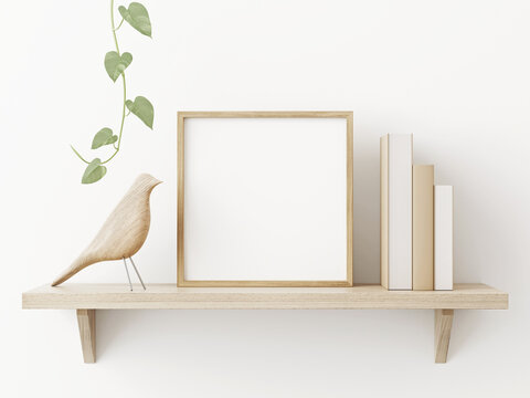Small square wooden frame mockup in scandi style interior with trailing green plant, bird, pile of books and shelf on empty neutral white wall background. 3d rendering, illustration