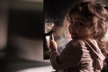 Cute little girl standing in front of a TV with broken screen holding a hammer. Home insurance...