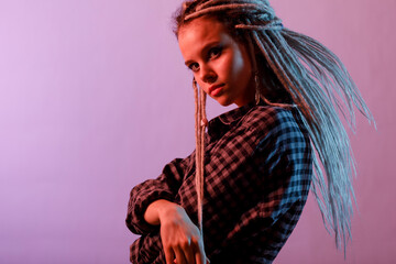A young, stylish woman in dreadlocks poses in a neon light. Fashion photo in color lighting.