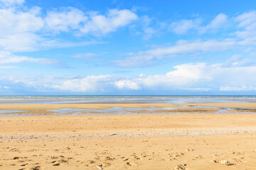 La plage de sable de Sword beach à Ouistreham sous un ciel avec des nuages en France, en Normandie, dans le Calvados, au bord de la Manche. - obrazy, fototapety, plakaty