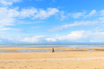 Fototapeta na wymiar Un homme marche sur la plage de Sword beach à Ouistreham sous un ciel avec des nuages en France, en Normandie, dans le Calvados, au bord de la Manche.
