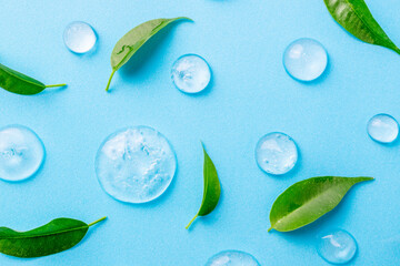 Cosmetics gel and green leaves on blue background. Texture of blue gel or sanitizer. Blue cosmetics gel for face cleansing. Moisturizing, beauty product, lotion, serum for skin care concept
