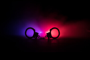 Police raid at night and you are under arrest concept. Silhouette of handcuffs with police car on...