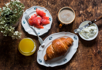 Delicious brunch - cappuccino, croissant, cream cheese, smoked salmon, orange juice on a wooden background, top view