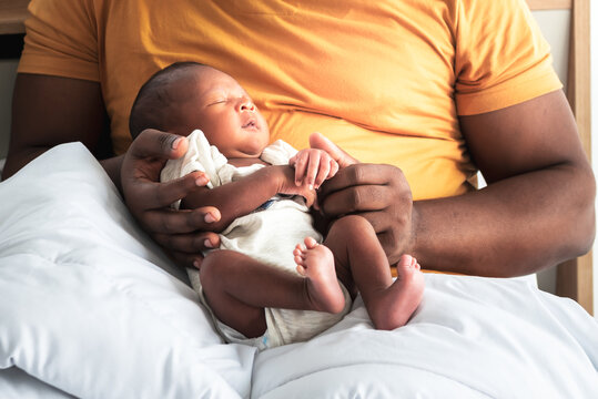 Portrait images of an African 12-day-old baby black skin newborn son, sleeping with his father being held, on the bed, to African family and infant newborn concept.