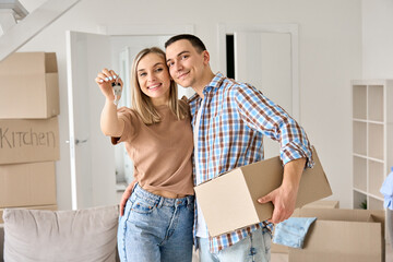Happy young couple home owners holding keys in new home. Smiling independent millennial man and...