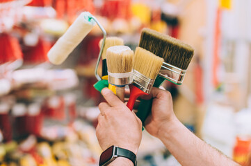 A man in a hardware store holds a set of brushes and rollers for paint and decor.