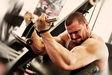 Fototapeta na wymiar Bodybuilding workout in gym. Powerful muscular man exercising biceps with full power on Scott's bench. Extreme expression in his face.