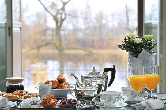 Rich breakfast serving on table with croissants, almonds, orrange juice and other pastry silverware autumn morning light