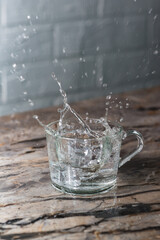 A splash of water in glass mug on the kitchen table. Clean and transparent. Lots of splashes