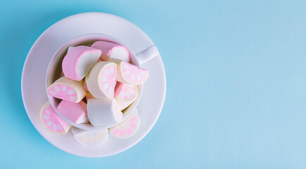 Colorful marshmallows in a white cup on a blue background. Fluffy marshmallow texture closeup.
