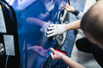 Car wrapping specialist putting vinyl foil or film on car. Selective focus.