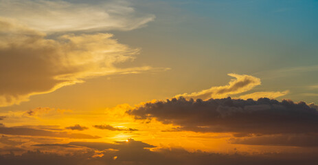 Picturesque colourful tropical sunset sky background or backdrop with yellow, orange and blue colors and heavy grey rainy clouds with sun looking though them. Horizontal orientation image