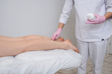 Laser epilation and cosmetology in beauty salon, spa concept. Preparation for the procedure of laser hair removal. Application of gel, disposable spatula. Beautiful smooth female legs