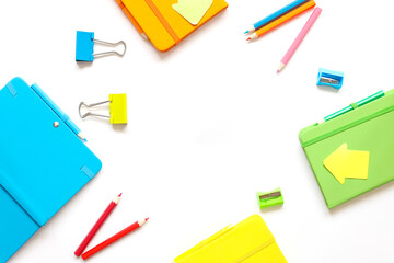 Stationary concept, top view Flat Lay Photo of stationery clips, pencils, notebooks in green blue yellow and orange. over white background with copy space. place for text in the center