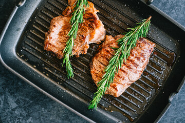 Grilled buffalo beef steak with rosemary in black grill pan on the table.