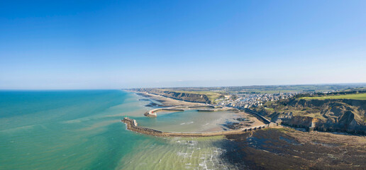 La vue panoramique de la plage, le port et la digue du port en Bessin en France, en Normandie, dans le Calvados, au bord de la Manche. - obrazy, fototapety, plakaty
