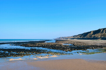 Fototapeta na wymiar La plage et les falaises du port en Bessin en France, en Normandie, dans le Calvados, au bord de la Manche sous le Soleil.