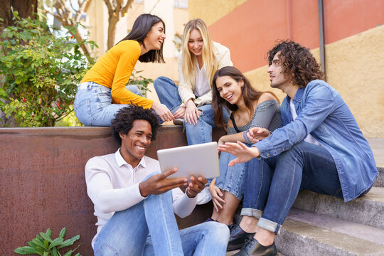 Multi-ethnic group of young people looking at a digital tablet outdoors in urban background.