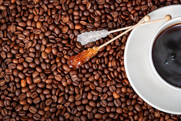 Coffee in a white cup and saucer with sugar sticks amongst coffee beans