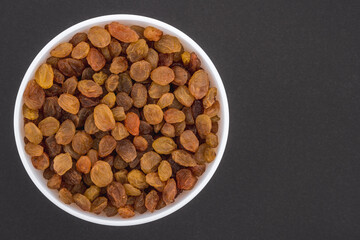 White glass bowl of yellow raisins Isolated on a dark grey background.