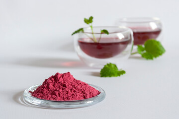 Pink matcha tea in bulk and brewed in glass cups with mint leaves on a white background.