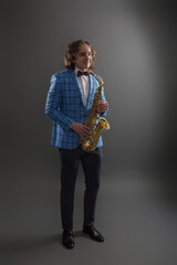 Full-length studio portrait of a young musician guy holding a saxophone.