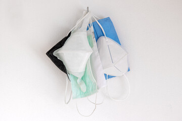 The used protective face masks hanging on a hook on a white wall, close up view