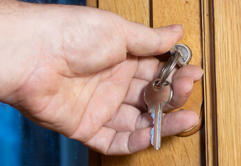Male hand puts the key in the keyhole. The key inserted in a wooden door lock, close up view.